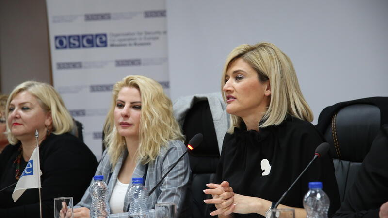 Three women speak at an OSCE Mission in Kosovo conference, seated at a panel table with microphones and water bottles.